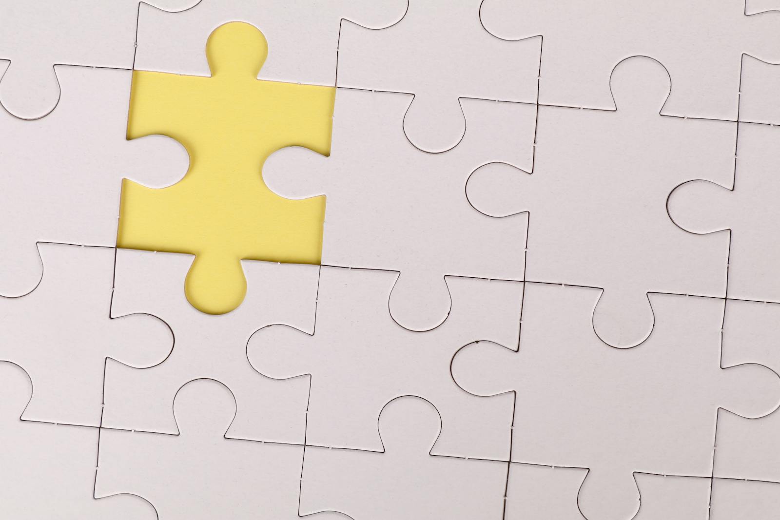 Close-up of a white jigsaw puzzle with a single yellow piece missing, symbolizing incompleteness.