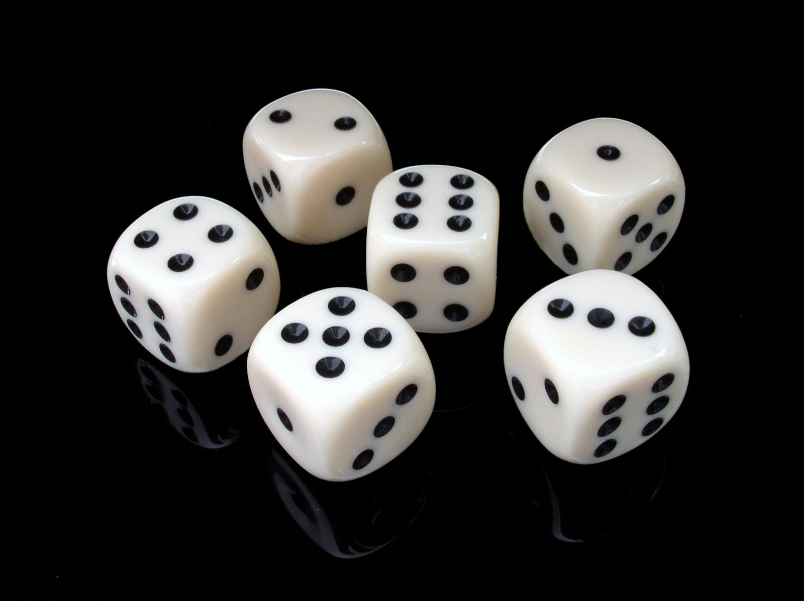 Set of white dice with black pips on a reflective black surface, showing various numbers.